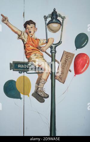 Ein Wandbild in der Ong Ang Walking Street von Klong Ong Ang, Chinatown / Phahurat, Bangkok, Thailand, das einen verspielten, fröhlichen Jungen auf einem Lampenpfosten zeigt Stockfoto