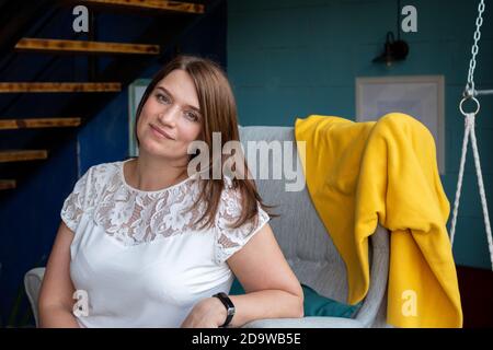 Schöne junge Frau mit roten langen Haaren in einer weißen Bluse, allein in einem Café auf einem Stuhl sitzend und auf ihre Bestellung wartend. Stockfoto