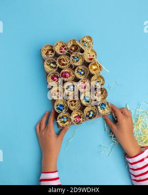 Kinder Hand Füllen Adventskalender mit Süßigkeiten, Draufsicht, blauer Hintergrund, Aktivität für Kinder Tutorial wie machen Toilettenrolle Handwerk für weihnachten, DIY, Schritt 3, Draufsicht, blauer Hintergrund Stockfoto