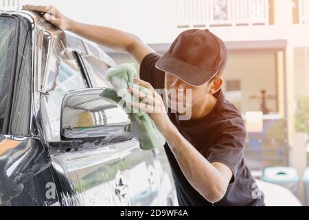 Autowascharbeiter mit T-Shirt und schwarzer Kappe reinigen das Auto in der Autowaschanlage mit einem Schwamm, Konzept für die Autopflege. Stockfoto