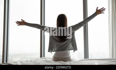 Rückansicht einer Frau, die in einem komfortablen Zimmer auf dem Bett saß Stockfoto