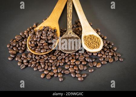 Kaffeebohnen, Kaffeepulver und Instant-Kaffee werden in einem Holzlöffel auf einer schwarzen Tischplatte platziert. Stockfoto
