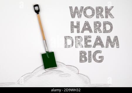 Work Hard Dream Big. Miniatur-Schaufel auf einem weißen Blatt Papier Stockfoto