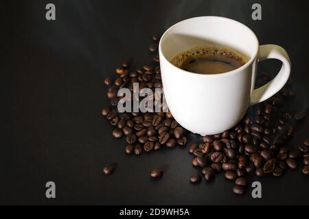 Heißer Kaffee aus weißem Keramikglas und Kaffeebohnen auf dem schwarzen Tisch. Stockfoto