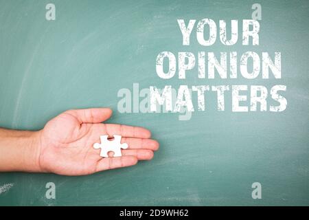 IHRE MEINUNG ZÄHLT. Stück weißes Puzzle in der Hand. Grüne Kreidetafel im Hintergrund Stockfoto