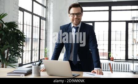 Porträt eines lächelnden Geschäftsmannes aus den 30er Jahren, der am Tisch im Büro steht. Stockfoto