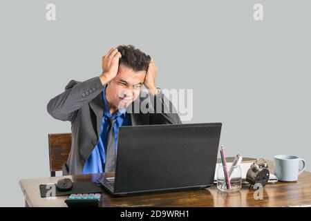 Ein junger Geschäftsmann, der einen Anzug trug, war schockiert, als er einen Laptop auf einem Schreibtisch in seinem Büro ansah, ein Konzept für Geschäftsleute. Stockfoto