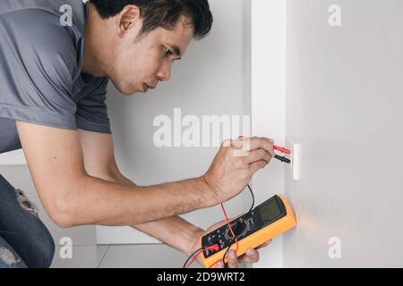 Elektriker verwendet ein digitales Messgerät, um die Spannung an der Steckdose in an der Wand zu messen. Stockfoto