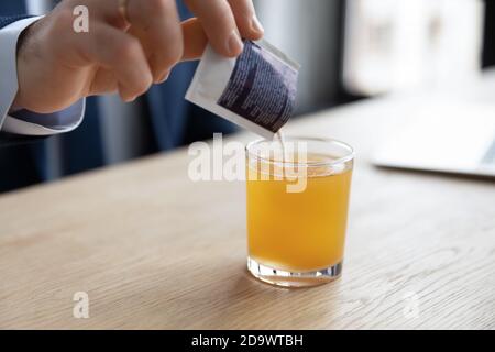 Junger Geschäftsmann gießt lösliches Anti-Influenza-Orangenpulver in Wasser. Stockfoto