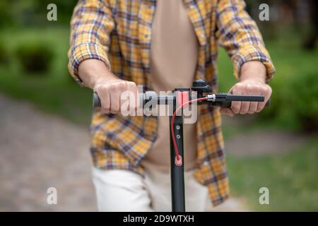 Motorroller fahren. Bild eines Mannes im karierten Hemd, der im Park einen Roller fährt Stockfoto