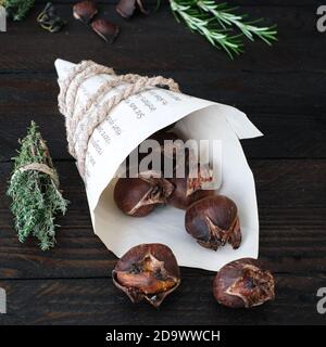 Frisch geröstete Kastanien, eingewickelt in einen Zeitungsbeutel, mit einer dicken Kordel gehalten, hübsch dekoriert auf einem dunklen Holztisch Stockfoto