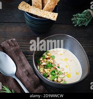 Frisch gekochte Kastaniensuppe in einer braunen Keramikschale, verziert mit Kastanienstücken und Petersilie auf einem braunen Holztisch mit Salz- und Pfefferstreuer, Stockfoto