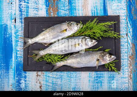 Roher Fisch (Blaufisch). Seefische, blaue Fische und Zitronen zusammen auf Holzhintergrund. Stockfoto