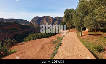 Wanderweg am Rande einer Schlucht über den Ouzoud-Fällen in Ouzoud, Marokko mit einer Ruhepause und Bergen im Hintergrund an sonnigen Tagen. Stockfoto