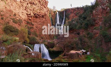 Vorderansicht des beliebten Touristenorts Ouzoud Falls in einer Schlucht in Ouzoud, Marokko mit Schuppen und Vegetation an einem sonnigen Tag. Stockfoto