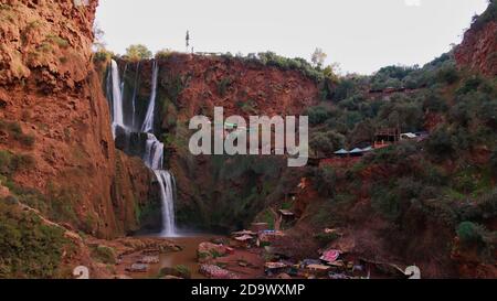 Panoramablick auf die beliebten Ouzoud-Wasserfälle (Wasserkaskaden) in einer Schlucht im Dorf Ouzoud, Marokko mit Booten, Souvenirläden für Touristen. Stockfoto