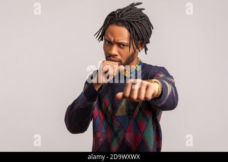 Zuversichtlich konzentrierte afrikanische Kerl mit Dreadlocks und Bart halten geballte Fäuste, bereit, einen Schlag zu machen, Schattenboxen, Selbstverteidigung. Studio im Innenbereich Stockfoto