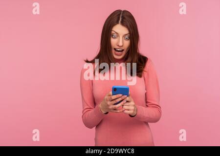 Aufgeregt Brünette Frau Blick auf Smartphone-Display in ihren Händen mit großen überrascht Augen, erhalten Nachricht über Boni und Rabatte. innenstudi Stockfoto