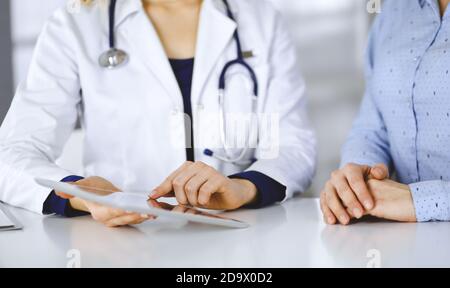 Unbekannte Ärztin zeigt ihrem Patienten eine Beschreibung der Medikation, während sie zusammen am Schreibtisch im Schrank in einer Klinik sitzt. Weiblich Stockfoto