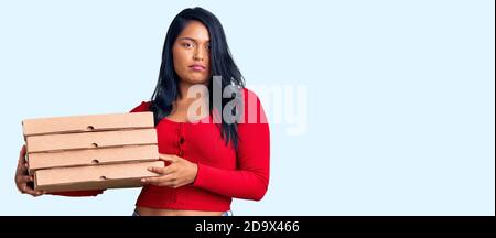 Hispanische Frau mit langen Haaren halten Lieferung Pizza Box denken Einstellung und nüchterner Ausdruck sehen selbstbewusst aus Stockfoto