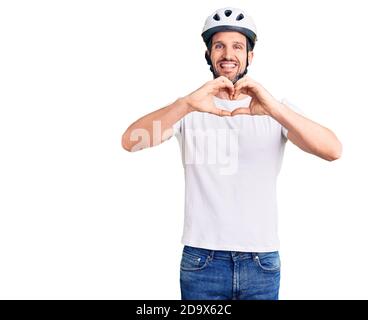 Junger schöner Mann trägt Fahrradhelm lächelnd in der Liebe tun Herz Symbol-Form mit Händen. Romantisches Konzept. Stockfoto