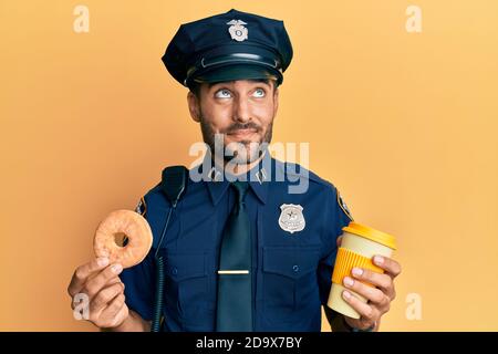 Gutaussehende hispanische Polizei Mann essen Donut und trinken Kaffee lächelnd Blick zur Seite und starrte weg denken. Stockfoto