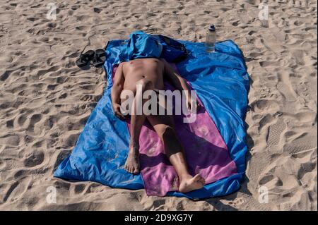 Ein Mann sonnenbaden, als er sich auf den Sand legt mit seinem Gesicht mit einem Hemd bedeckt am Shek O Strand, als die Regierung die Wiedereröffnung der öffentlichen Strände nach vier Monaten der Schließung inmitten Covid-19 Coronavirus Ausbruch in Hongkong angekündigt hat. Stockfoto