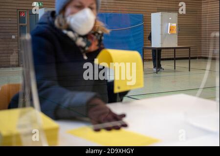 Stuttgart, Deutschland. November 2020. Ein Wahlhelfer mit Mund- und Nasenschutzmaske legt in einem Wahllokal einen Stimmzettel zur Wahl des neuen Oberbürgermeisters in Stuttgart auf einen Tisch. Im Hintergrund steht ein Mann in einer Wahlurne. Eine mögliche Abwahl findet am 29. November 2020 statt. Quelle: Sebastian Gollnow/dpa/Alamy Live News Stockfoto