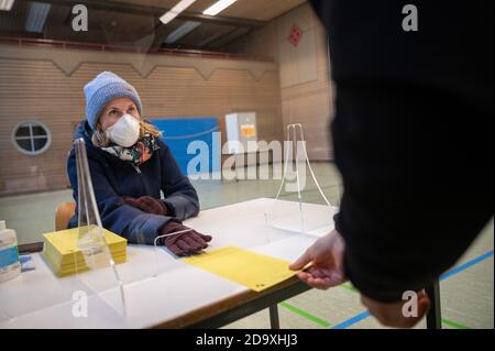 Stuttgart, Deutschland. November 2020. Ein Wahlhelfer mit Mund-Nase-Schutzmaske gibt einem Wähler eine Stimmabgabe zur Wahl des neuen Oberbürgermeisters in Stuttgart in einem Wahllokal. Eine mögliche Abwahl findet am 29. November 2020 statt. Quelle: Sebastian Gollnow/dpa/Alamy Live News Stockfoto