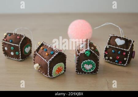 Kleine Häuser mit weißem Faden genäht. Rosa Lampe im Hintergrund auf einem Holztisch. Filz Weihnachten Hand genäht einzigartige Dekorationen. Stockfoto