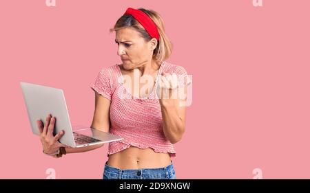 Junge blonde Frau mit Laptop genervt und frustriert schreien vor Wut, schreien verrückt mit Wut und die Hand angehoben Stockfoto