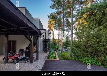 Blick auf den grünen Garten der Luxus-privaten Hütte in der Nähe eines Pinienwaldes. Außenansicht eines modernen Privathauses. Schaukel im Garten. Stockfoto