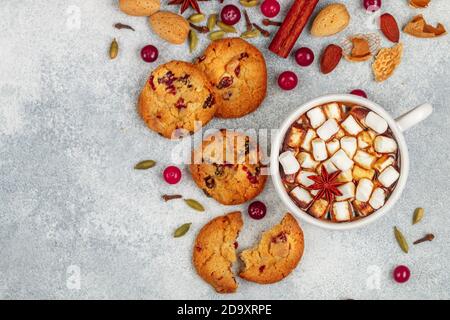 Heiße Schokolade (Kaffee, Kakao) mit Marshmallows in einer weißen Tasse und hausgemachte Kekse mit Preiselbeeren, Mandeln und Gewürzen (Zimt, Sternanis, Kardam Stockfoto