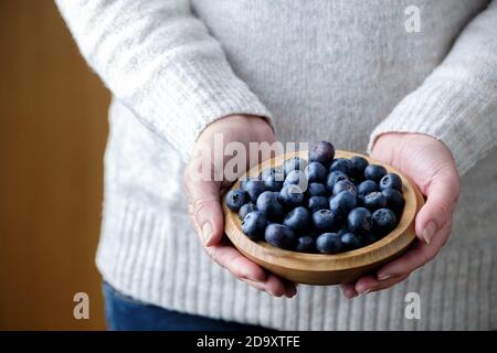 Eine Frau, die eine Holzschale mit frischen Blaubeeren hält, Cyanococcus. Die Heidelbeere ist eine reiche Quelle von Antioxidantien und reich an Vitaminen c und K. Stockfoto