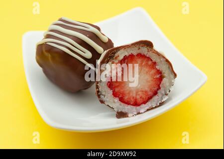 Schokoladenei (Osterei) Kokosnuss gefüllt mit Erdbeere in zwei Hälften auf einem Teller geschnitten. Isoliert auf gelbem Hintergrund. Nahaufnahme. Horizontale Aufnahme. Stockfoto