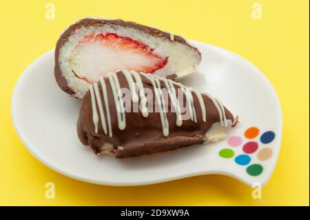 Schokoladenei (Osterei) Kokosnuss gefüllt mit Erdbeere in zwei Hälften auf einem Teller geschnitten. Isoliert auf gelbem Hintergrund. Stockfoto