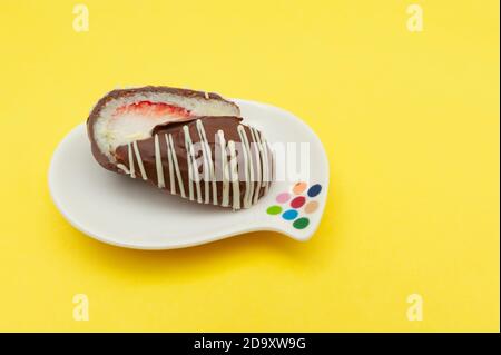 Schokoladenei (Osterei) Kokosnuss gefüllt mit Erdbeere in zwei Hälften auf einem Teller geschnitten. Isoliert auf gelbem Hintergrund. Speicherplatz kopieren. Stockfoto