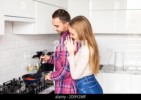 Junger Mann kocht mit Freundin und würzt die Sauce. Guy fügt schwarzen Pfeffer in Bratpfanne auf Herd, während Frau mit Spachtel zu mischen. Mult Stockfoto