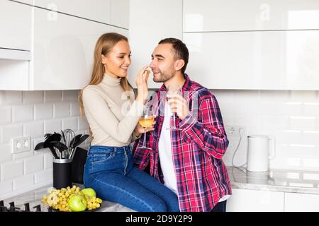 Liebevolles junges Paar mit Weingläsern, die in der Küche sitzen Stockfoto