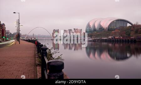 Frühmorgendliches Bild vom Quayside in Newcastle upon Tyne, das den Salbei, die Millennium Bridge und das Baltic Arts Centre zeigt, die sich im stillen Wasser spiegeln Stockfoto