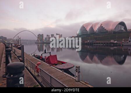 Frühmorgendliches Bild vom Quayside in Newcastle upon Tyne, das den Salbei, die Millennium Bridge und das Baltic Arts Centre zeigt, die sich im stillen Wasser spiegeln Stockfoto