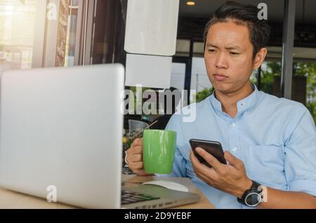 Asiatische Geschäftsleute halten ein Handy, betrachten Daten am Computer und sorgen sich um die Arbeit. Stockfoto