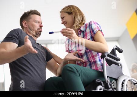 Frau im Rollstuhl glücklich lächelt Mann und hält Schwangerschaft Test Mann sieht überrascht. Stockfoto