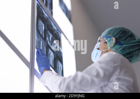 Arzt mit medizinischer Maske im Büro untersucht eine Röntgenaufnahme. Stockfoto