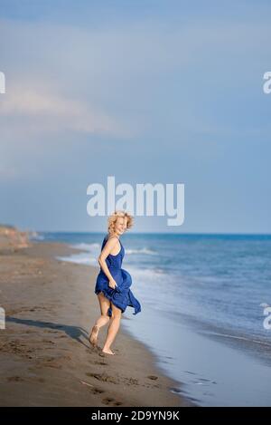 Ganzkörperportrait einer jungen Frau, die lacht und läuft Am Strand Stockfoto