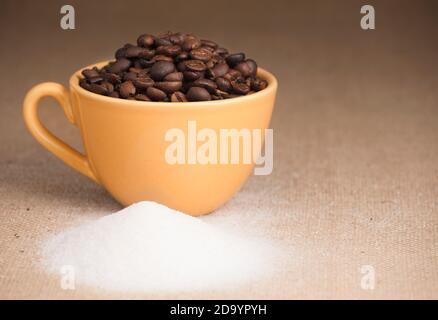 Gelbe Tasse Kaffee mit Getreide und Zucker, Bast Stoff Hintergrund Stockfoto