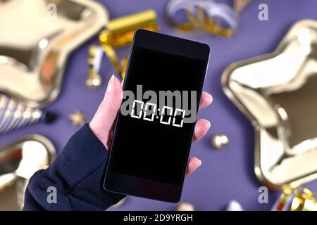 Silvester-Festkonzept mit Handgriff auf Smartphone Mit Timer Countdown bis Mitternacht vor Party-Elemente Im Hintergrund Stockfoto