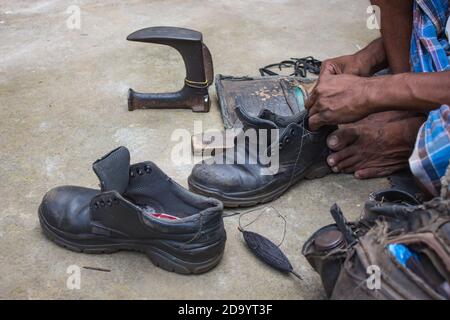 Indische lokale Schuster Reparatur Schuhe neben der Straße von Hand mit Werkzeugen in traditioneller Weise. Natürliche Schuss Darstellung der täglichen Arbeit eines regelmäßigen Schuster. Stockfoto