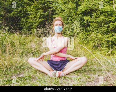 Ein Mädchen in einer Maske sitzt in der Natur und verbreitet sie Knie zu den Seiten und über ihre Arme Stockfoto