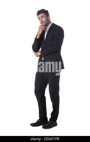 In voller Länge Porträt von jungen schönen Geschäftsmann in schwarz Anzug Denken Hand auf Kinn Studio isoliert auf weiß halten Hintergrund Stockfoto